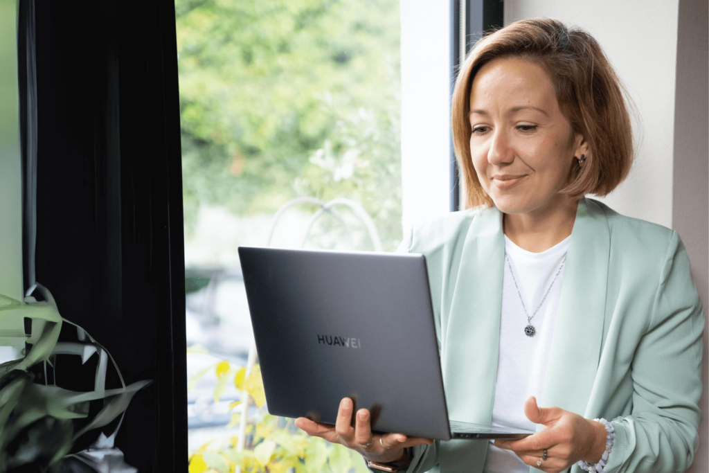 Irina Oczko, Freelancerin für SEO, sitzt am Schreibtisch mit einem Laptop in der Hand und schaut auf den Bildschirm und lächelt dabei