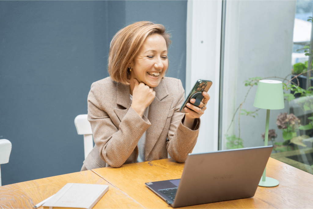 Irina Oczko, Freelancerin für Content Marketing, SEO und Social Media, sitzt am Schreibtisch mit Handy in der Hand und schaut auf das Handy und lächelt dabei